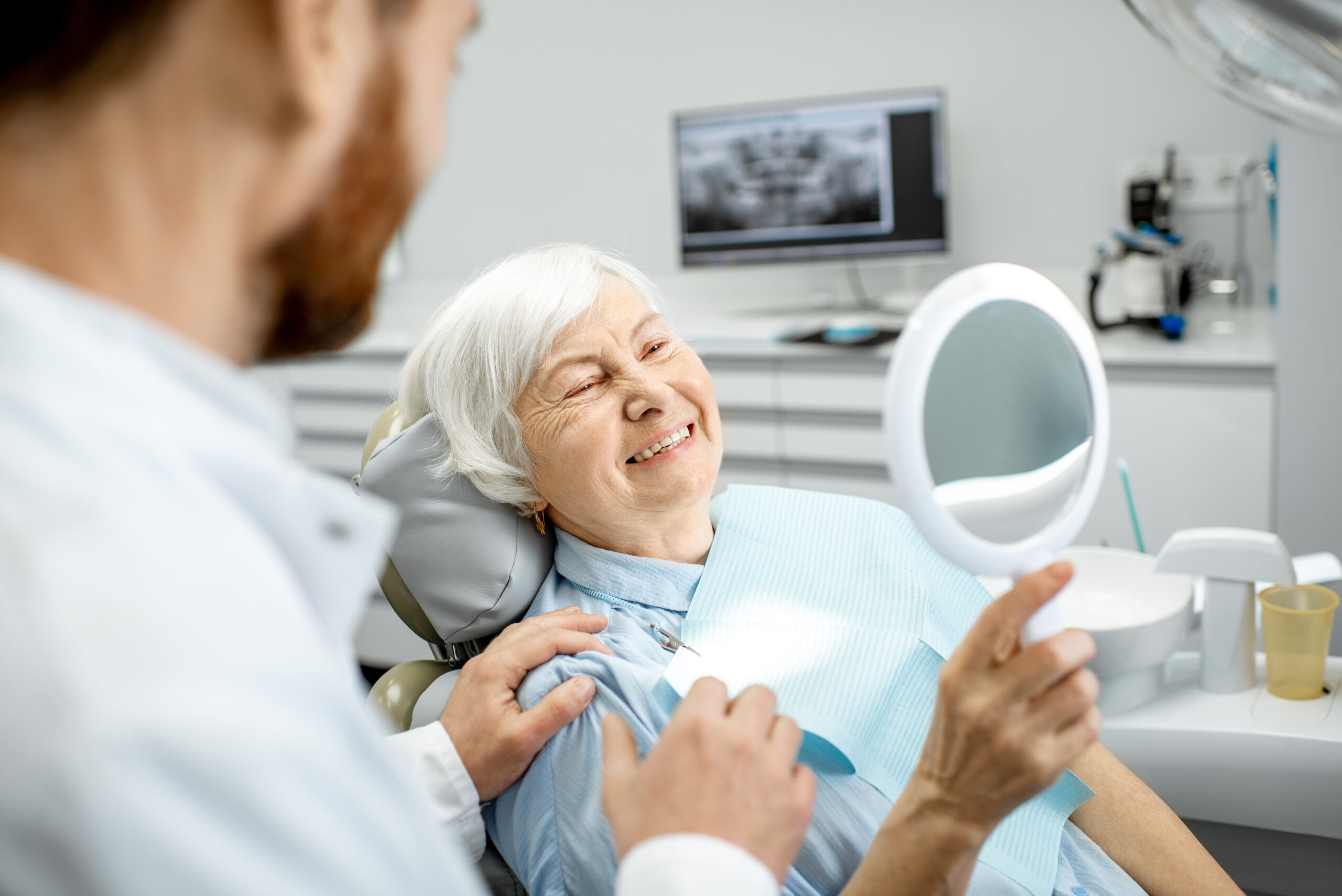 Elderly woman checking her beautiful smile in a mirror at a dental office